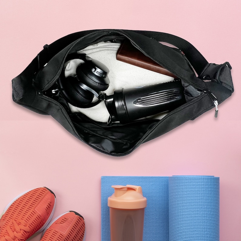 Puede incluir: Una bolsa de deporte negra con cierre de cremallera, que contiene una botella de agua, auriculares y una toalla. La bolsa est&aacute; abierta y el contenido es visible.