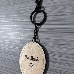 Peut inclure: Un porte-cl&eacute;s ovale en bois avec une cha&icirc;ne noire et un fermoir en m&eacute;tal noir. Le porte-cl&eacute;s porte les mots "So Much" grav&eacute;s avec un petit symbole de c&oelig;ur.