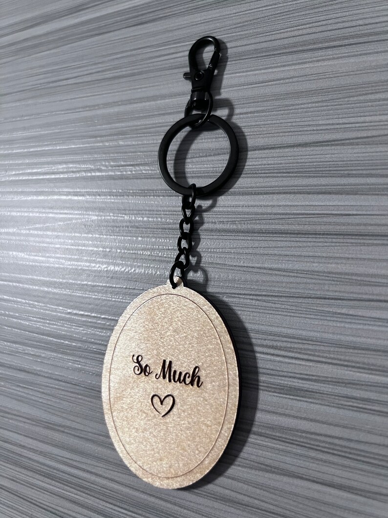 Peut inclure: Un porte-cl&eacute;s ovale en bois avec une cha&icirc;ne noire et un fermoir en m&eacute;tal noir. Le porte-cl&eacute;s porte les mots "So Much" grav&eacute;s avec un petit symbole de c&oelig;ur.