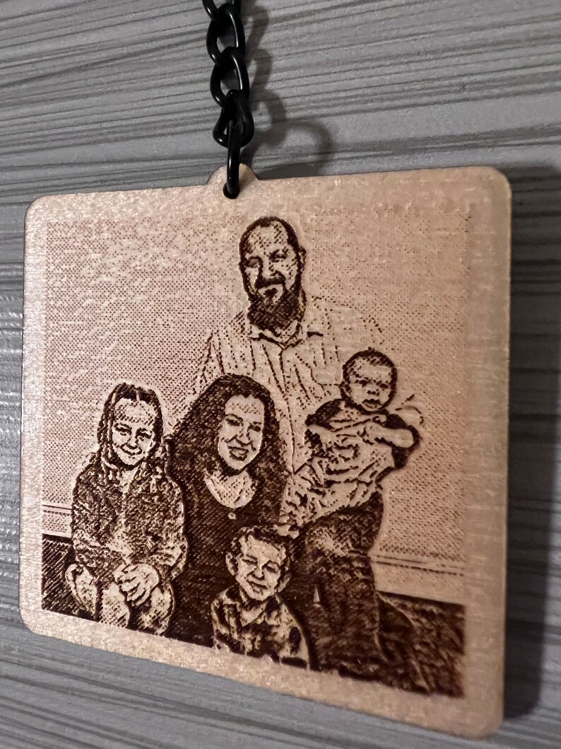 Peut inclure: Un porte-cl&eacute;s en bois avec une image grav&eacute;e au laser d'une famille de cinq personnes. La famille sourit et semble &ecirc;tre dans un cadre familial. Le porte-cl&eacute;s est attach&eacute; &agrave; une cha&icirc;ne en m&eacute;tal noir.
