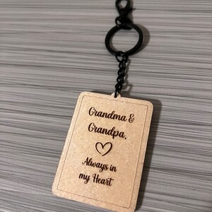 Peut inclure: Porte-cl&eacute;s en bois avec une cha&icirc;ne en m&eacute;tal noir et un motif en forme de c&oelig;ur. Le porte-cl&eacute;s porte la gravure "Grandma & Grandpa. Always in my Heart".