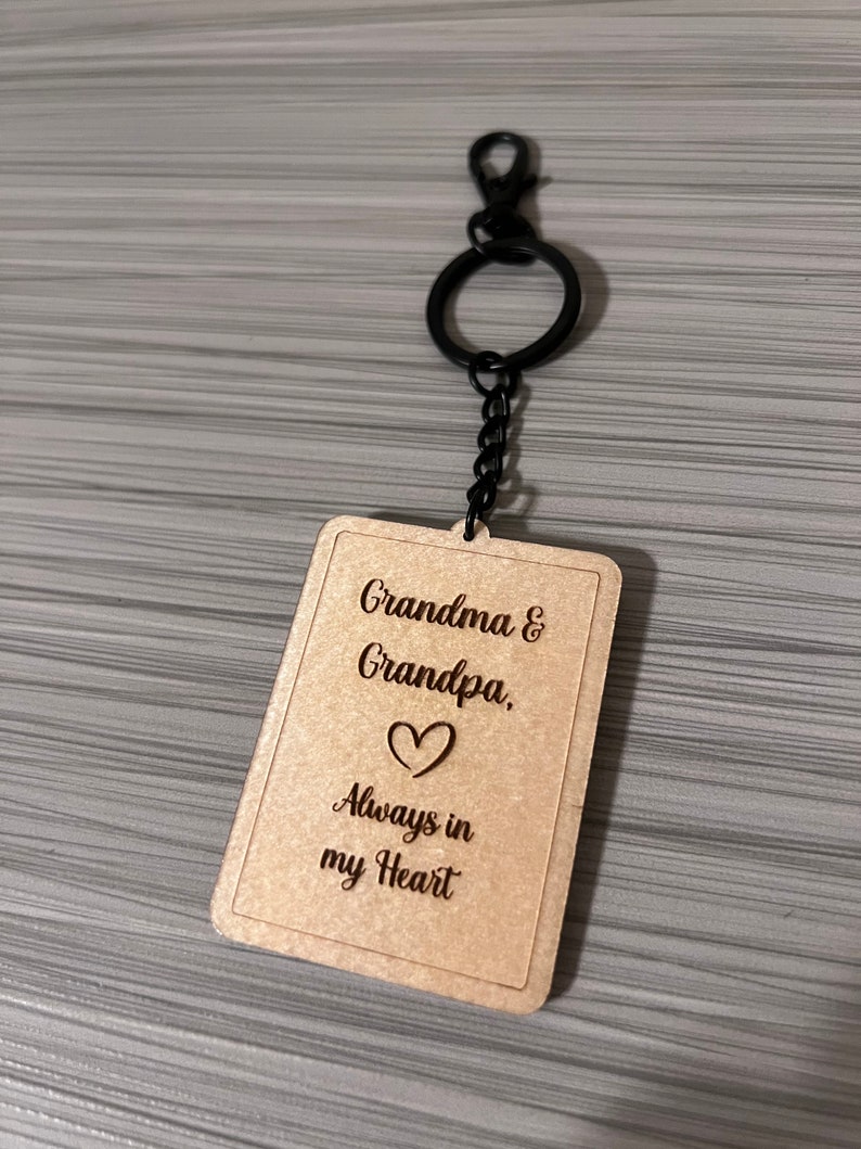 Peut inclure: Porte-cl&eacute;s en bois avec une cha&icirc;ne en m&eacute;tal noir et un motif en forme de c&oelig;ur. Le porte-cl&eacute;s porte la gravure "Grandma & Grandpa. Always in my Heart".