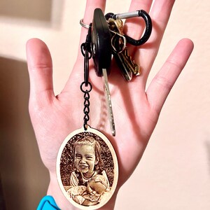 Peut inclure: Un porte-cl&eacute;s ovale en bois avec une photo grav&eacute;e au laser d'une jeune fille tenant un b&eacute;b&eacute;. Le porte-cl&eacute;s est attach&eacute; &agrave; une cha&icirc;ne noire et un jeu de cl&eacute;s.