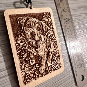 Peut inclure: Un porte-cl&eacute;s en bois avec une image grav&eacute;e au laser d'un chien brun. Le porte-cl&eacute;s est attach&eacute; &agrave; une cha&icirc;ne en m&eacute;tal noir.