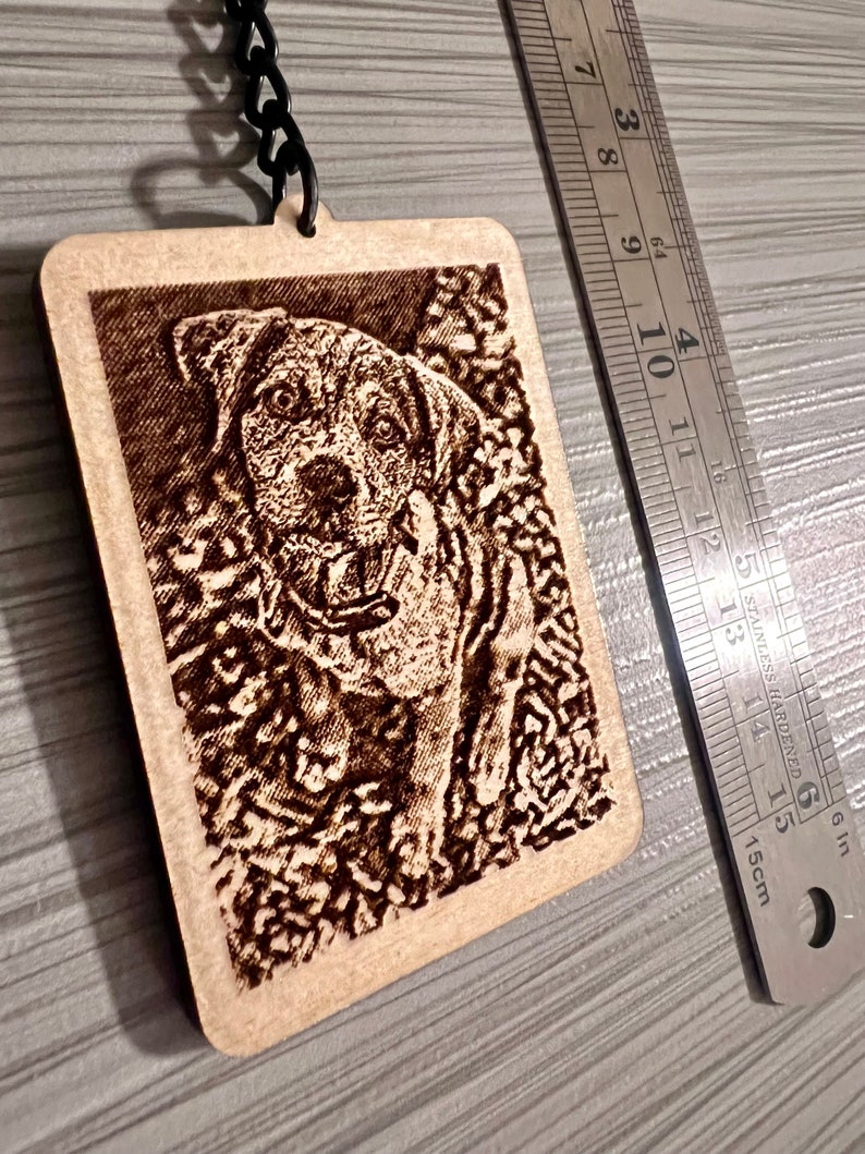 Peut inclure: Un porte-cl&eacute;s en bois avec une image grav&eacute;e au laser d'un chien brun. Le porte-cl&eacute;s est attach&eacute; &agrave; une cha&icirc;ne en m&eacute;tal noir.