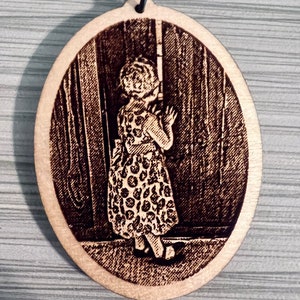 Peut inclure: Un porte-cl&eacute;s ovale en bois avec une image grav&eacute;e au laser d'une jeune fille en robe &agrave; pois debout devant une porte.