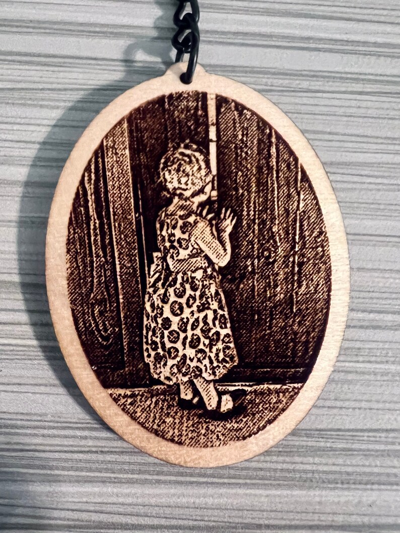 Peut inclure: Un porte-cl&eacute;s ovale en bois avec une image grav&eacute;e au laser d'une jeune fille en robe &agrave; pois debout devant une porte.
