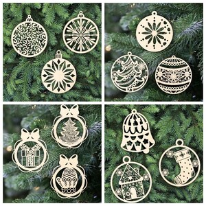 May include: A set of ten laser-cut wooden Christmas ornaments featuring various designs, including a snowflake, a Christmas tree, a bell, a stocking, a house, a mitten, a gift box, and a star. The ornaments are all in a light wood color and are arranged on a green pine tree background.