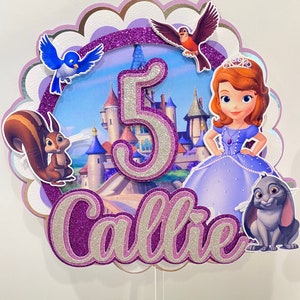 May include: Purple and silver glitter cake topper with a princess, a castle, a squirrel, a bird, a rabbit, and the number 5. The name Callie is written in glitter letters.