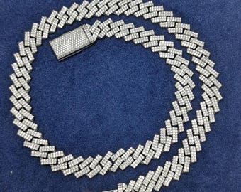 May include: A silver-toned chain necklace with a rectangular link design, encrusted with small, clear gemstones. The necklace features a secure clasp and lies on a dark blue surface, showcasing its intricate details and sparkling appearance.