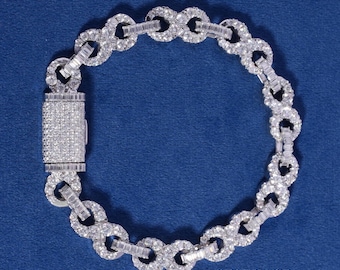May include: A diamond bracelet with a repeating circular link design. The bracelet features a rectangular clasp and is set against a blue background. The text "ICEDOUT DIAMOND" is visible in the lower right corner.