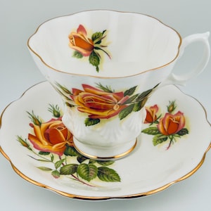 Könnte beinhalten: Ein weißes Tee-Set mit goldener Verzierung. Das Set zeigt ein Blumenmuster mit orangefarbenen und gelben Rosen.