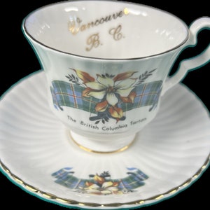 May include: White teacup and saucer with a gold rim. The cup and saucer feature a floral design with a plaid ribbon and the text "Vancouver B.C. The British Columbia Tartan".