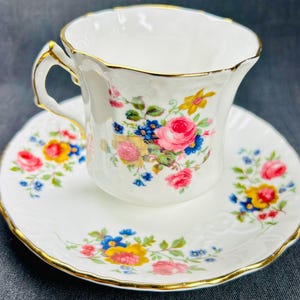 Peut inclure: Service à thé blanc composé d'une tasse et d'une soucoupe ornées de motifs floraux roses, jaunes et bleus. Les bords sont dorés. La tasse a une anse incurvée et repose sur une soucoupe assortie.