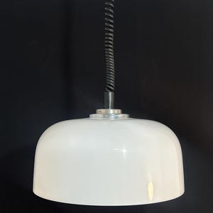 May include: A white, dome-shaped pendant light fixture with a silver-colored base and a black, coiled cord. The light hangs against a black background.