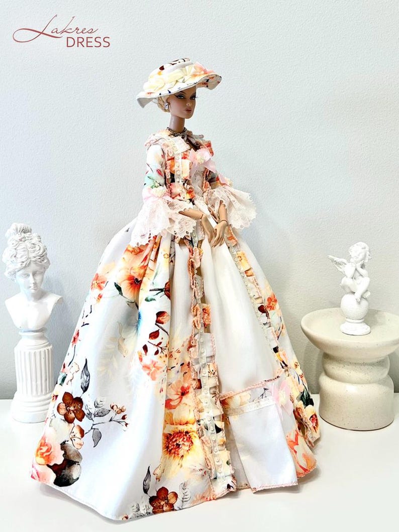 May include: A doll wearing a floral print dress and matching hat. The dress features a white background with orange, pink, and brown floral patterns. The doll is posed with a bust and small statue in the background. The text "Lakree Dress" is in the upper left corner.