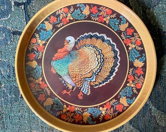 May include: A round serving tray with a tan rim and a dark brown center featuring a central illustration of a turkey with colorful plumage. The border is decorated with a repeating pattern of autumn leaves, acorns, and small red fruits.