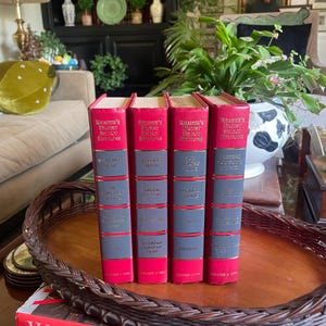 May include: Four vintage books with red spines and gray covers are displayed on a woven tray. The books are titled "Reader's Digest Select Editions" and feature titles like "We'll Meet Again" and "Running Blind". The books are part of a collection.