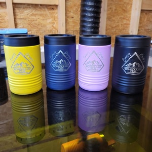 Peut inclure: Quatre porte-boissons isothermes en acier inoxydable avec une montagne et le texte "Scheduled Fun" grav&eacute; sur chacun. Les porte-boissons sont jaunes, bleus, violets et noirs.