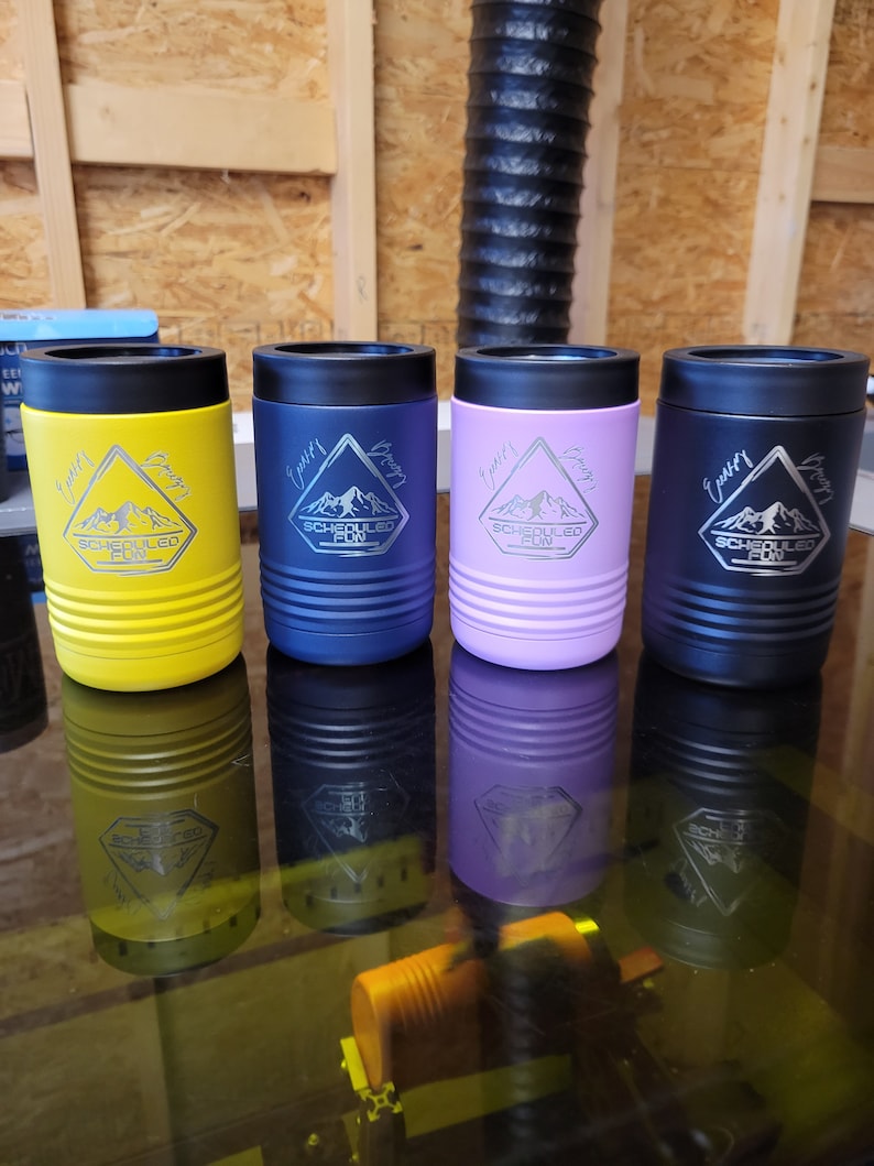 Peut inclure: Quatre porte-boissons isothermes en acier inoxydable avec une montagne et le texte "Scheduled Fun" grav&eacute; sur chacun. Les porte-boissons sont jaunes, bleus, violets et noirs.