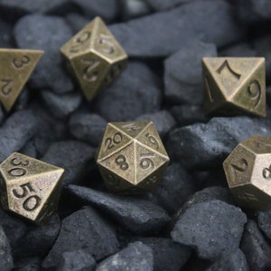 May include: A set of antique bronze-colored polyhedral dice for tabletop games. The dice are arranged on a bed of dark gray rocks. Each die has a different number of sides and is marked with numbers.