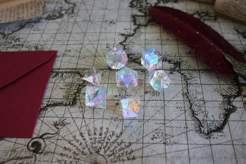 May include: A set of iridescent dice with gold numbers on a vintage map background. The dice are made of clear glass and have a rainbow effect.