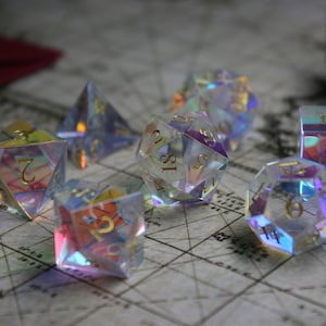 May include: A set of iridescent dice with gold numbers. The dice are made of clear glass and have a rainbow effect. The dice are on a map-like surface.