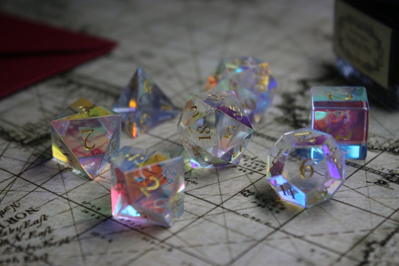 May include: A set of iridescent dice with gold numbers. The dice are made of clear glass and have a rainbow effect. The dice are on a map-like surface.