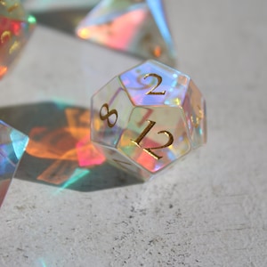 May include: A clear iridescent 12-sided die with gold numbers. The die is showing the number 12.