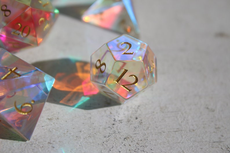 May include: A clear iridescent 12-sided die with gold numbers. The die is showing the number 12.