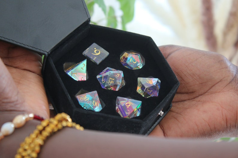 May include: A set of iridescent dice in a black velvet box. The dice are numbered 1 through 6 and have gold lettering. The box is hexagonal and has a black leather exterior.