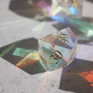 May include: A clear iridescent d20 dice with gold numbers. The dice is showing the number 30.