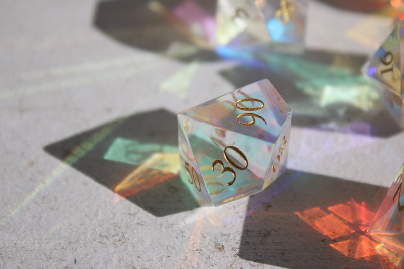 May include: A clear iridescent d20 dice with gold numbers. The dice is showing the number 30.