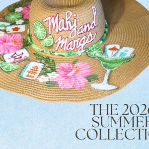 May include: A wide-brimmed straw hat with hand-painted tropical designs. The hat features pink hibiscus flowers, green lime slices, and the text "Mahi and Margs" on the brim. The hat also has a margarita glass design and the text "THE 2026 SUMMER COLLECTION".