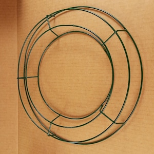 May include: A circular dark green wire wreath frame consisting of three concentric rings connected by four perpendicular crossbars. The structure is made of thin, coated metal wire and is designed to serve as a base for crafting floral arrangements.