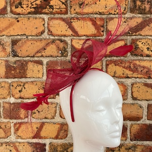May include: A red feather and mesh headband with a large bow. The headband is on a white mannequin head.