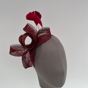 May include: A burgundy hat with a large bow and a feather accent. The hat is made of a delicate, woven material.