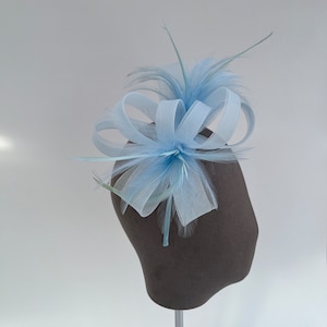 May include: A light blue feather and tulle hair accessory with a bow. The accessory is displayed on a brown mannequin head.