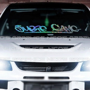 以下が含まれることがあります： スタイリッシュなフォントで「SUBRE GANG」の文字が入った、ホログラフィックカーのフロントガラスバナー。白い車に表示され、テキストは虹色です。車のヘッドライトとグリルが見えます。