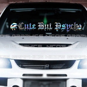 May include: A white car with a windshield decal that reads "Cute But Psycho" in a dripping, gothic font. The decal is iridescent and reflects a rainbow of colors.