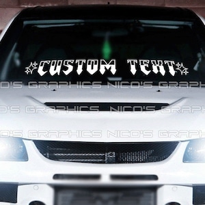 Könnte beinhalten: Weißer Auto-Windschutzscheibenaufkleber mit dem Text "CUSTOM TEXT" in einer stilisierten Schriftart mit Sternen auf beiden Seiten.