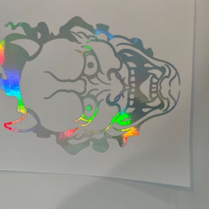 Könnte beinhalten: Holografischer Aufkleber mit einer detaillierten Illustration des Gesichts eines Fabelwesens. Das Design hat einen Regenbogen-Schimmer, mit leuchtenden Farben. Der Aufkleber ist in der Form des Designs geschnitten, geeignet für verschiedene Anwendungen.