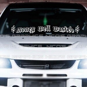 Könnte beinhalten: Ein weißes Auto mit einem schwarz-weißen Aufkleber auf der Windschutzscheibe, auf dem "$ money well wasted $" steht.