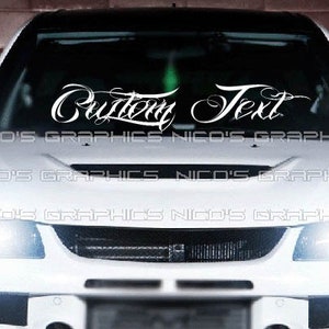 May include: White vinyl decal with the words "Custom Text" in a cursive font. The decal is applied to the windshield of a white car.