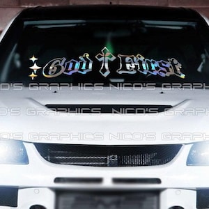 Puede incluir: Un coche blanco con una calcomanía en el parabrisas que dice "God First" en una fuente estilizada con una cruz. La calcomanía tiene un acabado holográfico iridiscente y detalles de estrellas.