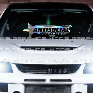 Puede incluir: Un coche blanco con una pegatina negra e iridiscente en el parabrisas que dice "ANTISOCIAL" en inglés y japonés. La pegatina tiene forma de estrella.