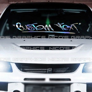 Peut inclure: Une voiture blanche avec un autocollant de texte personnalisé sur le pare-brise qui dit "Custom Text". L'autocollant est iridescent et a une police de style graffiti.