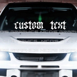 Könnte beinhalten: Weißes Auto mit einem benutzerdefinierten Text-Aufkleber auf der Windschutzscheibe, der "custom text" in einer gotischen Schriftart lautet.