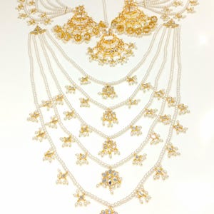Peut inclure: Un collier multi-rangs de perles avec des accents dorés et des motifs floraux pendants. Le collier est assorti à des boucles d'oreilles et à un maang tikka.