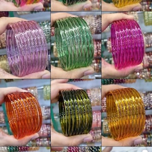 May include: A collection of colorful glass bangles in various shades, including green, yellow, pink, and orange. The bangles are stacked together, creating a vibrant display of accessories. The image showcases the bangles in different lighting conditions.